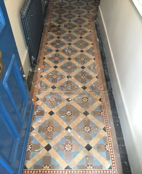 A view of a dirty and damaged Victorian hallway floor containing encaustic and plain blue and buff tiles